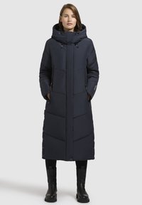 Long, dark navy puffer coat with a hood, featuring a zip closure, side pockets, and snap buttons along the hem. Smooth, quilted texture.