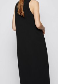 Černé šaty bez rukávů s volným střihem, vyrobené z hladké tkaniny a s vysokým výstřihem, s jednoduchým a minimalistickým designem.