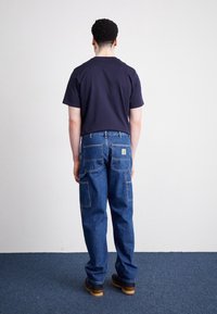 Tummansiniset farkut, rento istuvuus, joissa on kaksi takataskua ja logotarra. Yhdistetty lyhythihaiseen laivastonsiniseen T-paitaan.