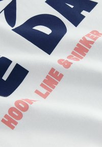 Valge kangas, millel on julged tumesinised ja korallpunased kirjad fraasiga "HOOK LINE & SINKER." Tekstuur näib pehme ja sujuv.