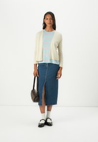 Cardigan beige, t-shirt rayé bleu, jupe en denim avec fente latérale, chaussures noires, chaussettes blanches et sac en bandoulière marron.