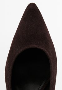Brown suede pointed-toe pump featuring a curved neckline, smooth black interior, and a sleek silhouette. No visible hardware or patterns.