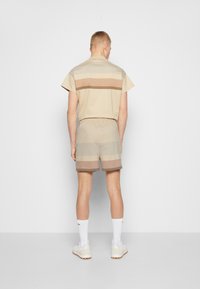 Beige kortärmad skjorta och matchande shorts med horisontella ränder i varierande nyanser av brunt. Elastisk midja, minimalistisk design.