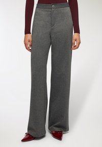 Szerokie spodnie w szary prążek o gładkiej teksturze, z zapięciem na guzik z przodu i pasem. Noszone z czerwonymi, spiczastymi butami.