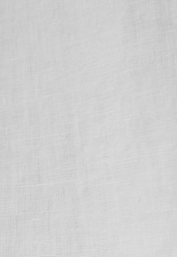 Gros plan d’une texture de tissu tissé blanc uni avec des fils visibles et un motif de tissage subtil.