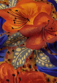 Lyse orange og blå tropiske blomster med mønstrede grå blade på tekstureret stofbaggrund med sorte prikkede accenter.