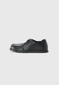 Black leather shoe with a rounded toe, low sides, and a textured finish. Features a simple lacing system and a flexible rubber sole.