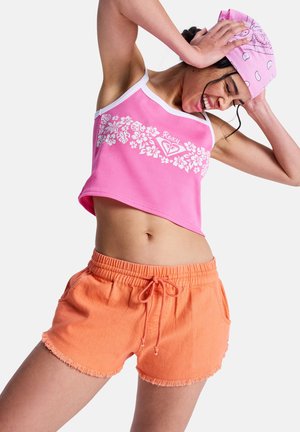 Różowy prążkowany krótki top z białym kwiatowym nadrukiem i logo, zestawiony z pomarańczowymi szortami na sznurku z frędzlowanymi brzegami. Oba elementy są swobodne i pełne energii.