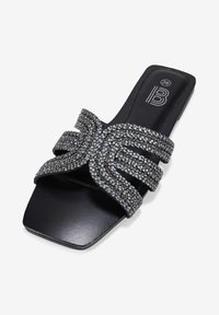 Infradito neri con suola piatta, dotati di tre cinturini intrecciati decorati con piccole borchie metalliche e una punta quadrata.