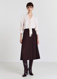 Blusa rosa chiaro con colletto a fiocco, abbinata a una gonna plissettata marrone scuro. Stivali al ginocchio lucidi in bordeaux completano l'outfit.