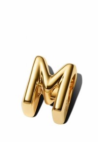 Bague de couleur or en forme de lettre "M" avec une surface lisse et réfléchissante et des bords arrondis. Remarquable pour son design audacieux et sa texture polie.