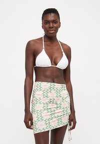 Hvit teksturert bikini topp med justerbare bånd, parret med et grønt omslagskjørt med et rosa blomstermønster og bølgete hvite detaljer.