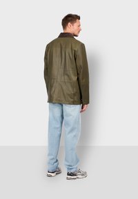 Olive green leather jacket with a brown collar, smooth texture, straight design, and two buttons at the base, worn with light blue jeans.