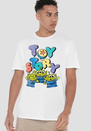 Junger Mann trägt ein weißes T-Shirt mit bunten "Toy Story" Ballonbuchstaben und drei grünen Außerirdischen in blauen Anzügen, die winken.