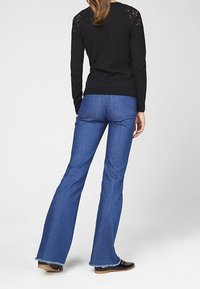 Musta pitkähihainen pusero, jossa pitsikoristuksia olkapäillä, yhdistetty sinisiin levenevillä lahkeilla varustettuihin farkkuihin, joissa on rispaantuneet reunat, ja ruskeisiin tasapohjaisiin kenkiin.