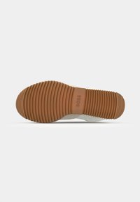 Sneaker con una suola in gomma marrone texture e parte superiore bianca. Presenta un dettaglio logo discreto e righe orizzontali per la trazione.