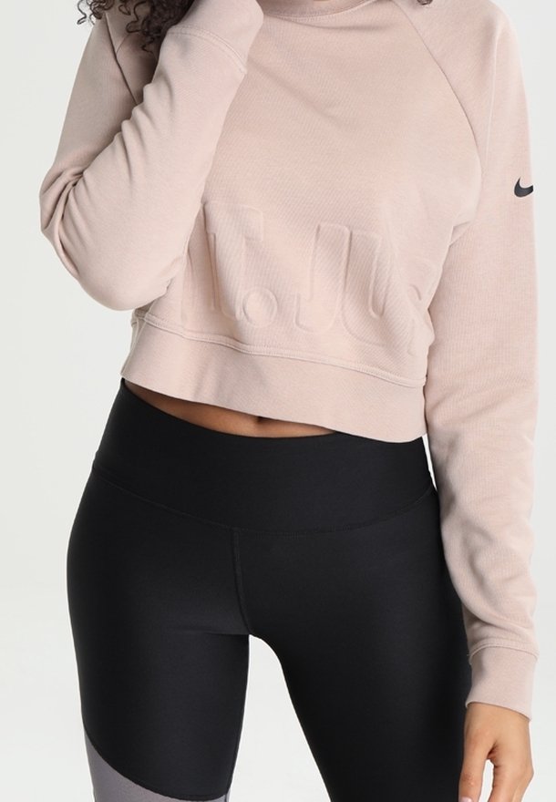 Sweat-shirt court rose clair avec logo texturé, associé à des leggings noirs taille haute avec des accents gris sur le bas des jambes.