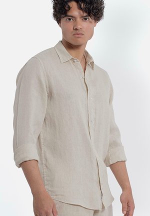 Camicia di lino beige con colletto button-down, maniche lunghe arrotolate fino ai gomiti e chiusura frontale con bottoni. Tessuto naturale con texture.