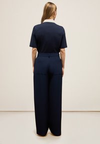 Marineblauw shirt met korte mouwen en een witte kraag, gecombineerd met marineblauwe wijde broek met achterzakken en een gladde textuur.
