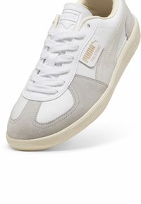Fehér sneaker szürke velúr részletekkel, texturált gumitalppal, kerek orral és fűzős záródással. Oldalán logóval.