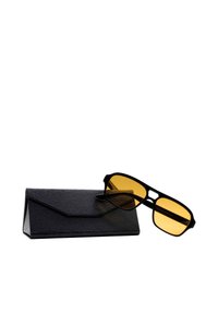 Occhiali da sole neri con lenti gialle, forma rettangolare, montatura in gomma, posizionati su un astuccio nero texturizzato con flap triangolare.