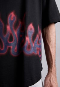 Crna majica s kratkim rukavima s grafikom crvenih i plavih plamenova duž ruba. Labav kroj. Mekana tkanina.