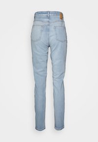 Jeans de denim azul claro com corte slim, apresentando dois bolsos traseiros e um patch de couro marrom na cintura. Textura suave e design clássico.