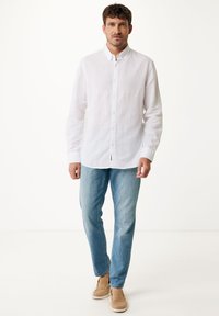 Witte linnen button-up shirt, lichtblauwe spijkerbroek en beige instappers. Het shirt heeft een klassieke kraag en lange mouwen.