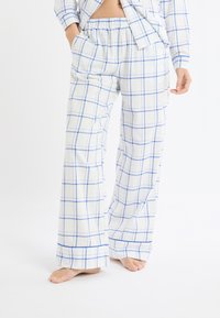 Pantalon de pyjama à carreaux blancs et bleus, doté d'une taille élastique, de poches latérales et d'une coupe décontractée avec des jambes légèrement évasées.