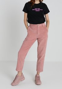 Pantalones de pana rosa con un corte recto, combinados con una camiseta negra de manga corta que presenta texto rosa. Complementados con zapatillas rosa claro.