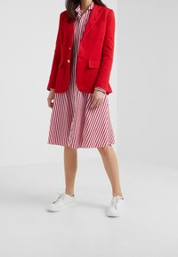 Czerwona marynarka z złotymi guzikami, w połączeniu z sukienką koszulową w czerwono-białe paski. Całość uzupełniają białe sneakersy. Gładki materiał, dopasowany krój.