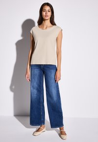 Beige kortärmad topp i kombination med vida blå jeans. Outfiten har en enkel design med mjuka texturer och en avslappnad passform.