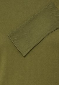 Gros plan d'une manche de pull en tricot vert olive reposant sur le corps du même pull, montrant le détail du poignet côtelé.