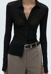 Schwarzes, geripptes Knopfhemd mit langen Ärmeln, kragenförmigem Design und leicht durchsichtigem Material. Kombiniert mit grauen Hosen und einem schwarzen Gürtel.