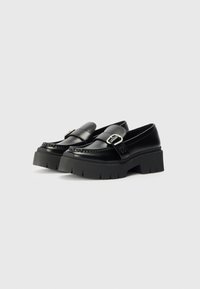 Sorte loafers med en kraftig plattformsåle. Laget av glatt lær, med en spenneaksent og sydd detaljer på fronten.
