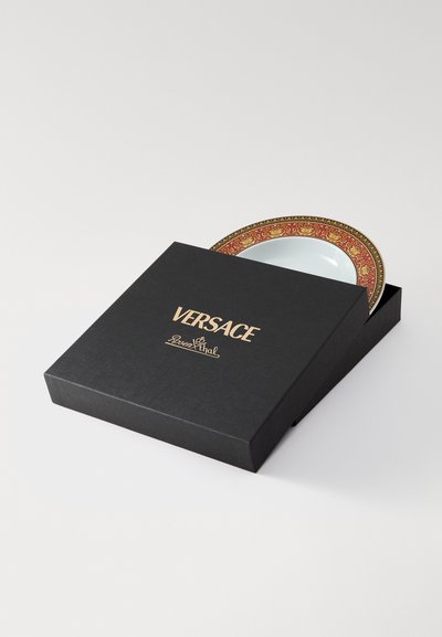 Prato Versace numa caixa preta, exibindo um prato branco circular com uma borda decorativa dourada e vermelha. Caixa rotulada com "Versace" em texto dourado.