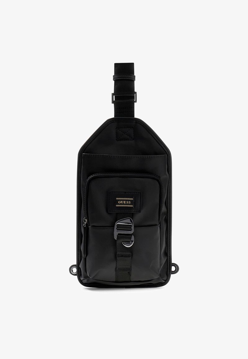 Sac en nylon noir de forme rectangulaire, avec une poche zippée à l'avant, une sangle réglable et un logo en patch doré. Texture lisse, design minimaliste.