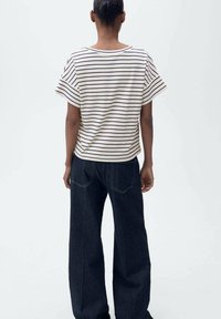 Randig kortärmad t-shirt i krämfärg och marinblå, kombinerad med vida mörka denimjeans med bakfickor och synliga sömmar.