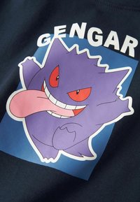Mørk marineblå t-skjorte med en lilla tegneseriefigur med røde øyne og stort glis, med navnet «Gengar» tydelig over.