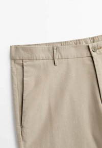 Beżowe bawełniane spodnie z przednimi kieszeniami, szlufkami na pasek i zapięciem na guzik na białym tle.