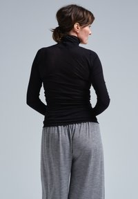 Schwarzes Langarm-Turtleneck-Oberteil aus einem weichen, dehnbaren Material, kombiniert mit lässigen, hellgrauen Hosen mit elastischem Bund.