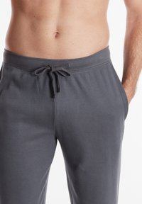 Pantaloni del pigiama grigi realizzati in tessuto texturizzato con vita elastica e coulisse regolabile. Presentano tasche laterali per maggiore comodità.