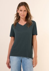 T-shirt a maniche corte e scollo a V di colore verde scuro, realizzato in un materiale morbido; vestibilità rilassata con una texture liscia e senza motivi o accenti visibili.