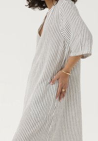 Robe en lin rayée blanc et marine, avec décolleté en V, coupe ample et manches courtes. Poches latérales et texture subtile mettent en valeur le tissu.