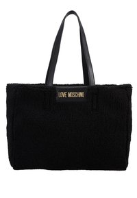 Svart tygväska med en strukturerad, fluffig yta, svarta läderhandtag och en guldlogoplåt. Rektangulär form med sydda detaljer.