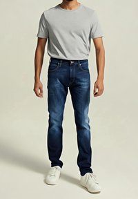 Mörkblå denimjeans med slim fit, kombinerat med en ljusgrå t-shirt. Skorna är vita sneakers. Minimalistisk design och slät textur.