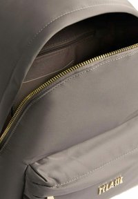 Primo piano della tasca anteriore dello zaino grigio aperta, che mostra la cerniera dorata e un scomparto interno con zip foderato in tessuto.