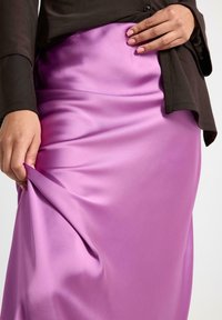 Person iført en sort langærmet top og trækker i stoffet på et skinnende lilla satin nederdel.