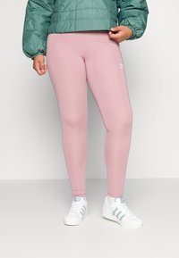 Ljust rosa leggings gjorda av stretchigt tyg med en smal passform. Kombineras med en grön vadderad jacka och vita sneakers med blå detaljer.