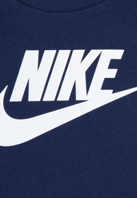 Laivastonsinisestä puuvillaisesta t-paidasta löytyy rohkea valkoinen "NIKE"-teksti ja ikoninen Nike-hyppynuotio dynaamisessa designissa.